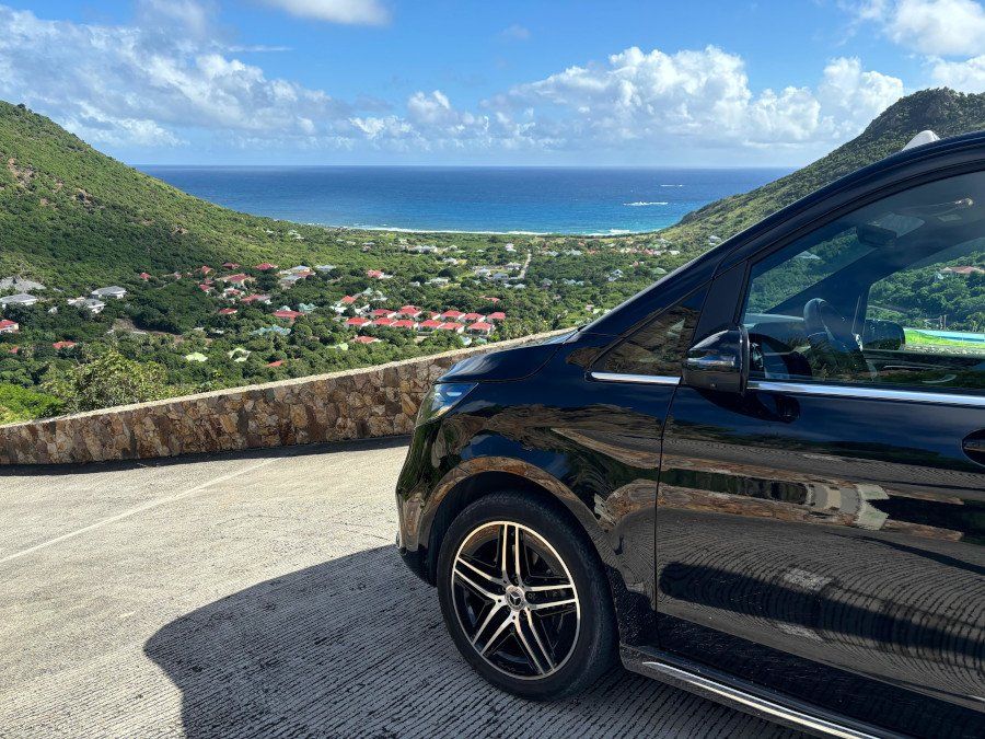 A private transfer van parked on a hillside road above a bay in St Barts